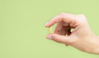 A woman's hand holds a green pill isolated on a green background. Natural vitamins and supplements. Close-up. Copy space. Selective focus. photo
