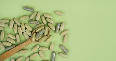 Natural vitamins and supplements in a wooden spoon on a green background. Top view. Close-up. Copy space. photo