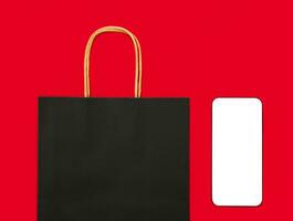 Shopping black bag and smartphone with a blank white screen on the red background. Mock up screen. Flatlay. Top view. Flatlay. Copy space. photo