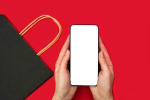 Woman's hands hold a smartphone with a blank white screen on the red background. Mock up screen. Buying goods online.Top view. Copy space. photo