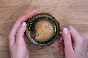 mujer manos sostener un taza de Fresco café a el cafetería. parte superior vista. de cerca. selectivo enfocar. foto