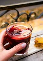 Woman's hand holds a glass of hot mulled wine in the street cafe. Seasonal hot drinks. Close-up. Selective focus. photo
