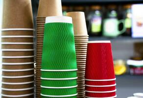 A stack of colorful disposable paper cups in a cafe. Paper cups from kraft paper for various drinks. Close-up. Selective focus. photo