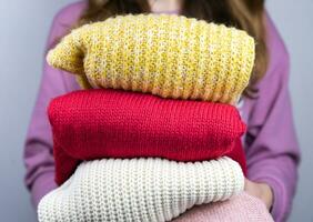 Woman holds warm knitted sweaters. Closet cleaning. Seasonal clothes. Donations. Close-up. Selective focus. photo