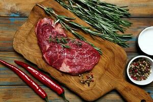 Raw organic beef meat with rosemary, seasonings, salt and red pepper  on wooden cutting board photo