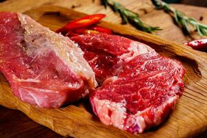 carne de res orgánica cruda con romero, condimentos, sal y pimiento rojo en tabla de cortar de madera foto