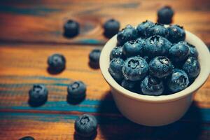 Freshly picked juicy blueberries in the bowl on wooden background, close up photo