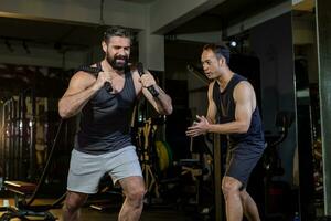 caucásico hombre con fuerte y muscular cuerpo formación en núcleo peso formación por cuerda tracción con su secundario entrenador alentador dentro gimnasio para avanzar ejercicio y rutina de ejercicio concepto foto