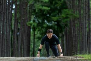 Asian trail runner is running outdoor in pine forest dirt road for exercise and workout activities training while concentrate on the start position to race for healthy lifestyle and fitness photo