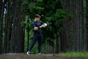 Asian trail runner is running outdoor in pine forest dirt road for exercise and workout activities training while checking smart watch on calories loss achieve healthy lifestyle and fitness photo