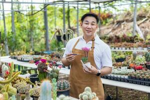 Asian gardener is working inside the greenhouse full of cactus plants collection while propagating by flower pollination for seed using small paint brush in ornamental garden and hobby concept photo