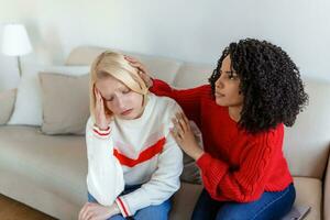 Friend trying to calm down her friend. Woman crying. Young lady sharing her problem with friend. female in depression. Woman omforting hes sad friend sitting on a couch in the living room at home photo