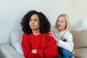 Two female friends sitting on sofa and arguing with each other. Friendship, quarrel, female disagreement, copy space. Angry couple or roommates sitting on a sofa in the living room at home photo