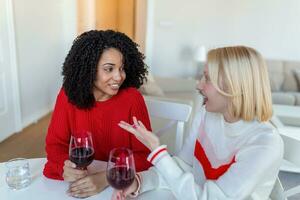 Women sitting on sofa laughing in a cozy loft apartment with wine. Two Female Friends Relaxing On Sofa At Home With Glass Of Wine Talking Together. photo