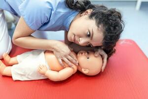 CPR practitioner examining airway passages on infant dummy. Model dummy lays on table and two doctors practice first aid. photo