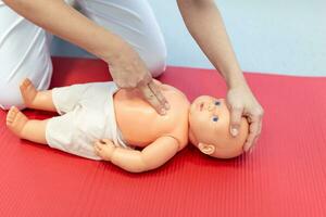 Woman performing CPR on baby training doll with one hand compression. First Aid Training - Cardiopulmonary resuscitation. First aid course on cpr dummy. photo