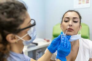 Medical worker wearing personal protective equipment doing corona virus swab on female patient - Covid19 test and health care concept photo