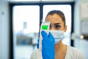 A pandemic workplace environment. Office workers wear face coverings to protect the spread of virus doing the Covid-19  Coronavirus outbreak. Body temperature is checked with a infrared thermometer. photo