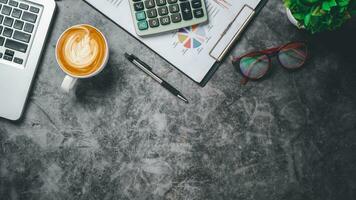 Office desk table with analysis chart or graph, pen, cup of coffee and calculator on dark background. Top view with copy space. Working desk table concept. photo