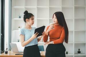 dos alegre joven multinacional colegas hablando mientras en pie en oficina con digital tableta, negocio concepto. foto