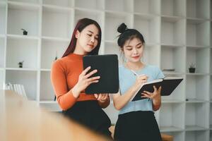 dos alegre joven multinacional colegas hablando mientras en pie en oficina con digital tableta, negocio concepto. foto