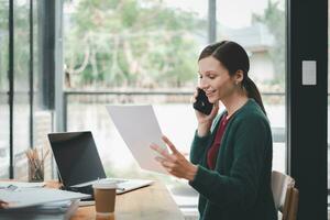 Happy businesswoman talking on mobile phone while analyzing weekly schedule in her notebook. photo