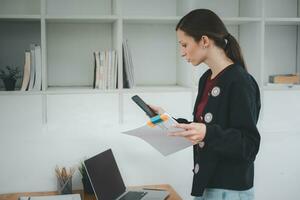 Attractive young woman talking on the smart phone and smiling while standing in office. photo