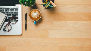 Top view, Wooden Office desk with laptop computer, cup of coffee, pen, eyeglass and notebook, copy space, Mock up. photo