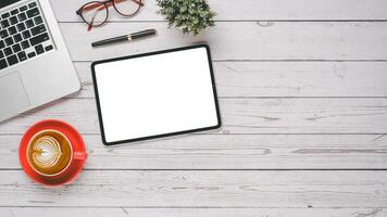 White wooden desk workplace with blank screen tablet, laptop, pen, eyeglass and cup of coffee, Top view flat lay with copy space. photo