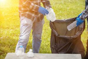 Two man employees use black garbage bags to collect plastic bottles and recyclable waste from the lawn and sidewalks for recycling. Concept of sorting plastic waste for recycling photo