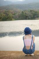 young woman sits alone on a path by a reservoir, lonely and depressed after living alone for so long. The back of a woman sitting by the reservoir alone in the evening and with a copy space for text. photo