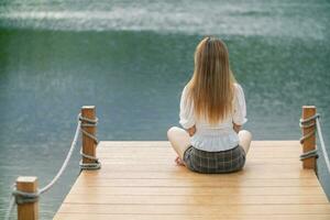 young woman sits alone on a path by a reservoir, lonely and depressed after living alone for so long. The back of a woman sitting by the reservoir alone in the evening and with a copy space for text. photo