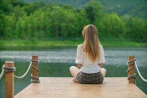 young woman sits alone on a path by a reservoir, lonely and depressed after living alone for so long. The back of a woman sitting by the reservoir alone in the evening and with a copy space for text. photo