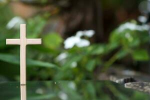 cross representing God in Christianity is placed on mirror and its reflection can be seen on blurred background of nature. cross on background is blurred and there is Copy Space on side for text. photo