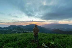 Male tourists stand on top of a mountain in the morning looking at the beautiful view of the twilight as the sun rises on the horizon and praying to God for blessings according to the Christian faith. photo