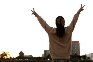 silhouette of young woman raising her hands above her head and making hand sign with two raised fingers that signifies victory and encouragement. Encouragement concept with victory and freedom symbols photo