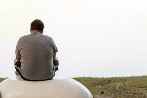 A depressed young man sat by the reservoir alone with a depressed feeling. The young man sat by the reservoir, depressed and staring into the water with emotional strain. Copy Space for text. photo