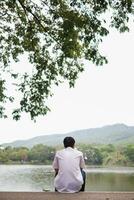 A depressed young man sat by the reservoir alone with a depressed feeling. The young man sat by the reservoir, depressed and staring into the water with emotional strain. Copy Space for text. photo