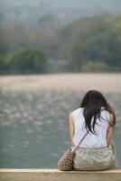 young woman sits on walkway by reservoir watching beautiful scenery of reservoir alone in the evening. back of woman sitting by reservoir alone in evening and with copy space for text. photo