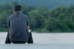 A depressed young man sat by the reservoir alone with a depressed feeling. The young man sat by the reservoir, depressed and staring into the water with emotional strain. Copy Space for text. photo