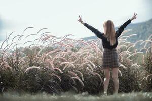 A young woman in a long sleeved black shirt and short skirt happily raises her hands above her head after exploring nature and grass field in the evening because the air is fresh. Copy Space for text photo