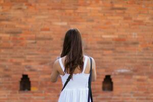 Asian tourists traveling and taking in sights of ancient city wall in Chiang Mai, Thailand, alone in summer. Back view of young female tourist taking walk taking in view of city wall and copy space photo