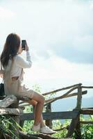 Back view of young woman sitting on long bench alone in evening looking at beautiful summer landscape background of nature and with copy space for text. concept loneliness of woman who is alone photo