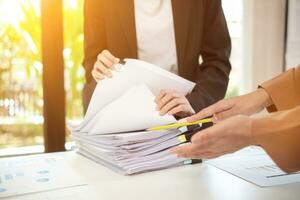 mujer de negocios manos trabajando en pilas de papel documentos a buscar y revisión documentos apilado en mesa antes de enviando ellos a tablero de directores a utilizar correcto documentos en reunión con empresario foto