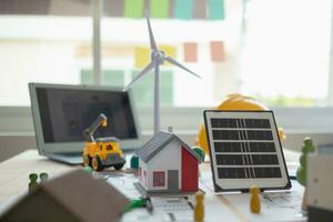 On desk of engineers lay model of house And solar panels to use in planning installation of solar panels to  house in order to get most cost effective energy from installing solar panels. photo