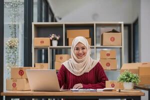 musulmán mujer en línea Tienda pequeño negocio propietario vendedor empresario embalaje paquete enviar Envío caja preparando entrega paquete o empaquetar en mesa. comercio electrónico soltar Envío envío Servicio concepto. foto