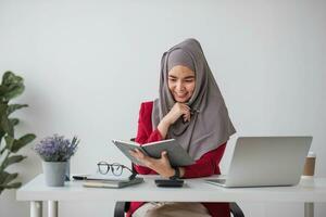 retrato de hermosa musulmán mujer de negocios sonriente a el cámara, sentado a su escritorio. foto