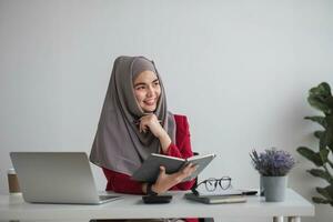 retrato de hermosa musulmán mujer de negocios sonriente a el cámara, sentado a su escritorio. foto