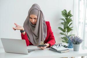 Serious young woman wearing hijab sitting at desk working on new business project alone in modern office photo