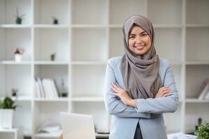 A portrait of a beautiful and professional Asian Muslim businesswoman stands in the office with her arms crossed. photo